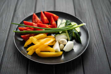 Vegetables cut into pieces on a plate on a black background, assorted tomatoes, cucumbers, peppers and onions on a black plate
