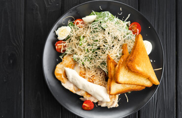 Traditional Caesar salad with grilled chicken, tomatoes, cheese and croutons on black background. Top view.