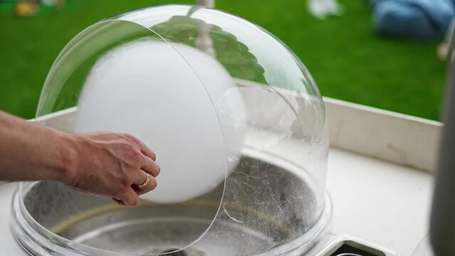 The hand deftly winds fluffy cotton candy around a wooden stick.