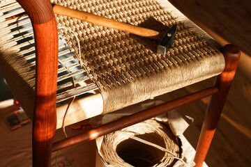 A carpenter weaving a new seat for a vintage danish chair with paper cord handcraft in a workshop