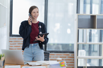 Beautiful young, concentrated businesswoman wearing shirt using smartphone while standing in modern workspace.