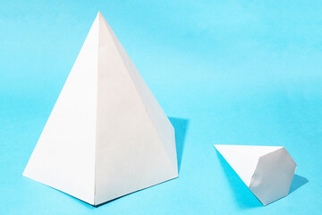 hand-crafted paper big standing and little lying pyramids on turquoise blue background