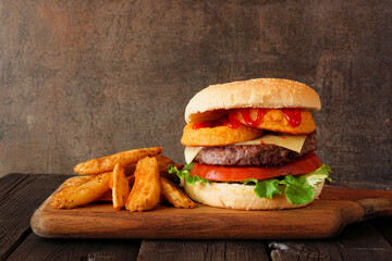 Onion ring hamburger with potato wedges. Side view table scene against a dark background.