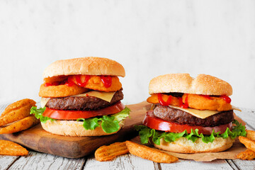Onion ring hamburgers with potato wedges. Side view table scene against a white wood background.