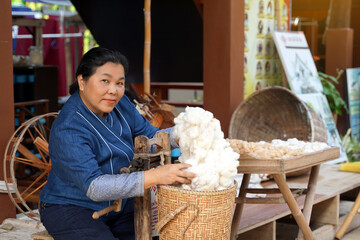 Asian woman hands picking up cotton in a bamboo basket spun by a Wooden Roller Giner. Soft and...