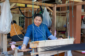 Asian female weavers weaving traditional patterns with hand weaving machines.in the concept of OTOP, community products, hand weaving fabrics, community shops, community weaving centers.