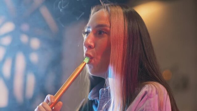 Close up of woman smoking shisha while hanging out in lounge bar with friends
