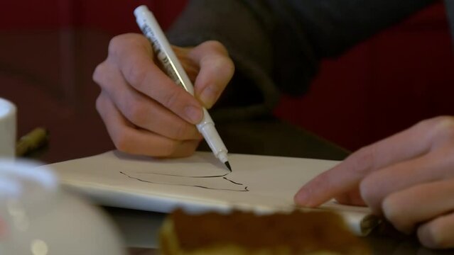 Girl artist draws in a cafe, in the foreground is a piece of tiramisu