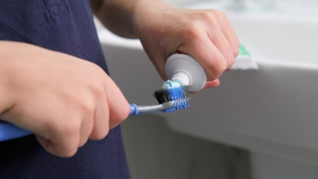 kids hands squeeze toothpaste onto toothbrush in bathroom at home, Health care, dental hygiene.