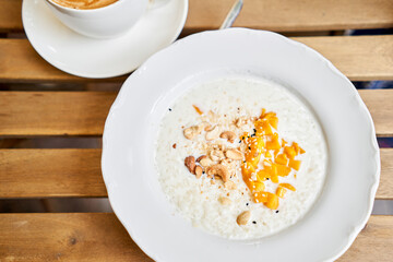 Breakfast in cafe on a sunny morning, on the summer veranda. Cappuccino coffee and rice porridge with mango, Cashews, sesame seeds. enjoying breakfast.