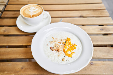 Breakfast in cafe on a sunny morning, on the summer veranda. Cappuccino coffee and rice porridge with mango, Cashews, sesame seeds. enjoying breakfast.
