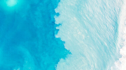 Top view of light blue water with white sand. Waves raise sand and a mix with turquoise water is obtained. Shadows from clouds on a clear ocean. Clear sea. Gradient of blue. The background photo