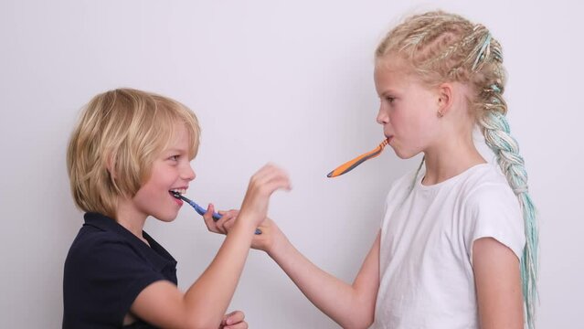 Portrait two kids having fun brushing teeth each other, happy smiling children kids boy and girl with toothbrush on white, looking at camera, Health care, dental hygiene.