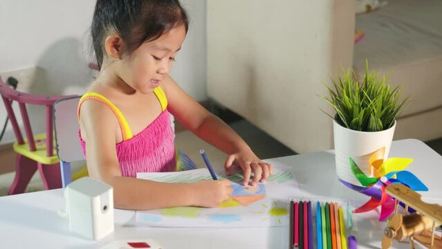 Asian cute kid preschooler sit on table smile she draw country house picture with pencil at home to learning arts homework, Happy child little girl colorful drawing landscape my home dream on paper