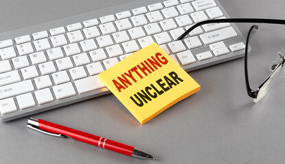 ANYTHING UNCLEAR text on a sticky with keyboard, pen glasses on grey background