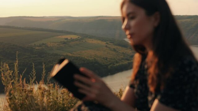 A girl reads the Bible in the open air. A woman holds a Bible in her hands and studies the word of God while sitting in a field at sunset