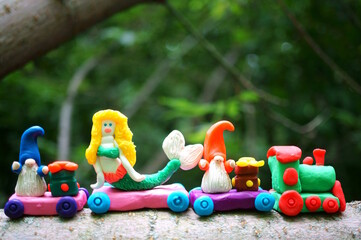 A toy train made of plasticine with a mermaid, gnomes and gifts. Children's toy decorations for the holiday and New year.