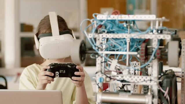Schoolgirl in the VR headset checking the work of the moving robot with a joystick in a class at a robotics lesson. Concept of technological modern education