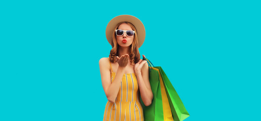Beautiful young woman posing with shopping bags wearing summer straw hat on blue background
