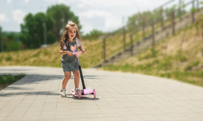 Child riding scooter. little girl rides a pink scooter on the road in a park outdoors on a summer day, active children playing outdoors, a healthy lifestyle concept for children