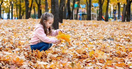 Positive little girl playing in the autumn park. Happy emotional child catches maple leaves and laughs. active holiday in autumn. leaf fall