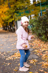 Positive little girl playing in the autumn park. Happy emotional child catches maple leaves and laughs. active holiday in autumn. leaf fall