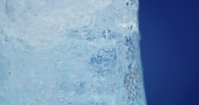 Ice cubes rotating in a glass with crystal clear water on a blue background. Refreshing and healthy water on hot days.