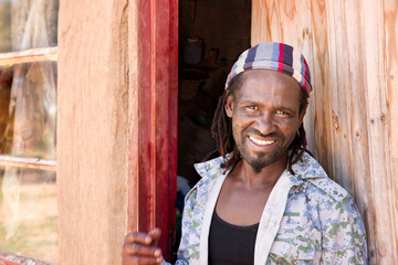 a Rastafarian village man with dreadlocks standing in front of the window of his house
