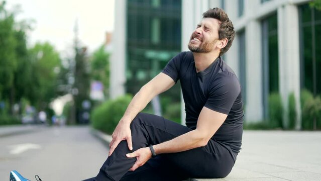 Athletic man massages a sprained leg injury during a workout run outdoor. Mature runner with muscle pain, trauma while jogging Fitness male sprain severe stretch pull. Leg muscle cramp calf sport