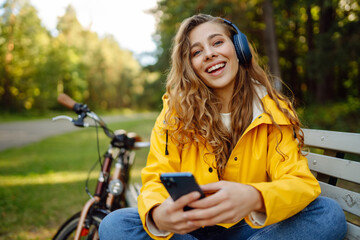 Fototapeta na wymiar Beautiful woman with headphones and smartphone rides a bicycle listening to music. Active lifestyle, vacation, resting. Communication in social networks. Lifestyle.