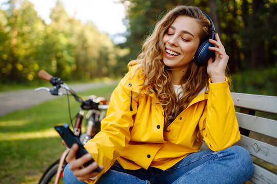 Beautiful woman with headphones and smartphone rides a bicycle listening to music. Active lifestyle, vacation, resting. Communication in social networks. Lifestyle.