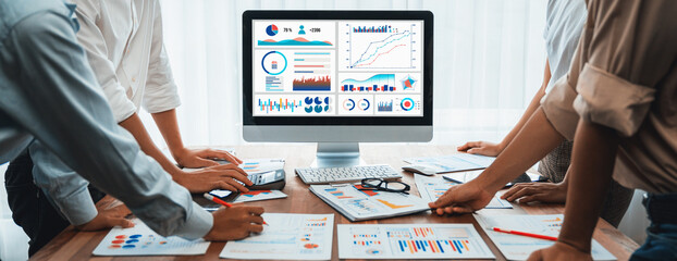 Analyst team utilizing BI Fintech to analyze and pointing at financial dashboard paper office. Businesspeople examining report paper on table for business insight. Panorama shot. Scrutinize