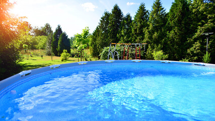 Swimming pool with metal frame for home and garden. Frame swimming pool in the yard. Garden in the background. Summer holiday fun and recreation.