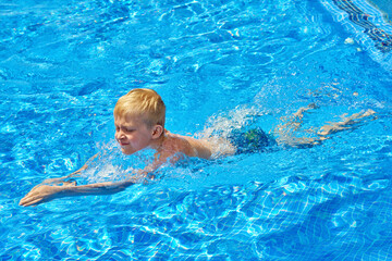 Fototapeta na wymiar Young boy kid child eight years old splashing in swimming pool having fun leisure activity. Boy happy swimming in a pool. Activities on the pool, children swimming and playing in water, happiness and