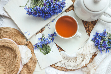 Cup of tea, open book and cornflowers, top view