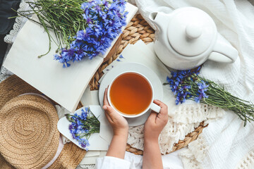A cup of tea in hands on a background of cornflowers, top view, aesthetic photo