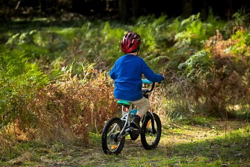 Fototapeta premium A little boy riding a bike on the grass wearing a red helmet and blue jacket