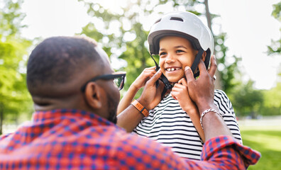 Happy family: father puts on son helmet for safe cycling in park