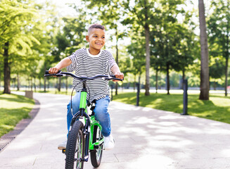 happy ethnic boy riding bike in park in summer