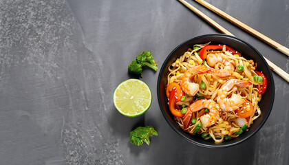 Stir fry noodles with vegetables and shrimps in black bowl. Slate background. Top view. Copy space.