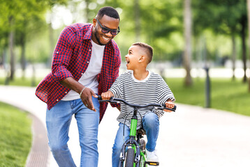 Happy ethnic family father teaches child  son  to ride bike in park - 623921120