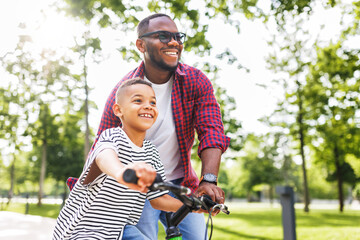 Happy ethnic family father teaches child  son  to ride bike in park