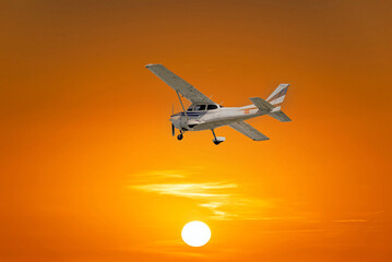 Single engine ultralight airplane flying under an orange sky at sunset