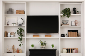 Modern TV set and shelves with decor near white wall. Interior design