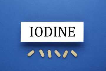 Card with iodine element and pills on blue background, flat lay