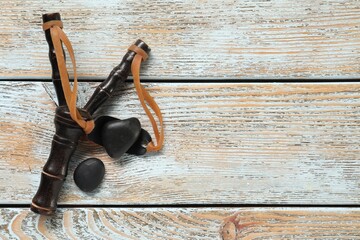 Black slingshot with stones on old light blue wooden table, flat lay. Space for text