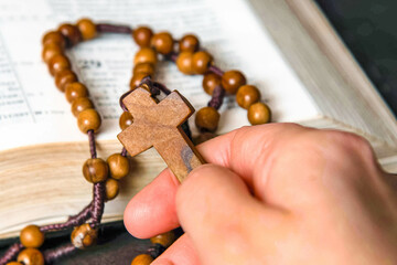 Fototapeta premium Hand holding and praying on rosary, on Bible background