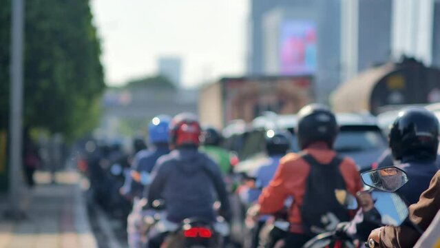 A blur image of Jakarta's urban traffic density dominated by motorcycles with skyscrapers in the background. Depicts high pollution, heat, congestion, and inequality. Taken with a telephoto lens.