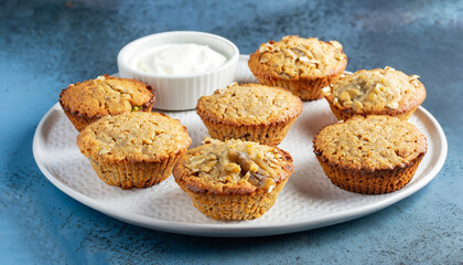 Obraz na płótnie Canvas Healthy vegan oat muffins, apple and banana cakes with sour cream on a white plate Blue stone background