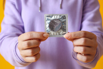 Young woman with condom on orange background, closeup